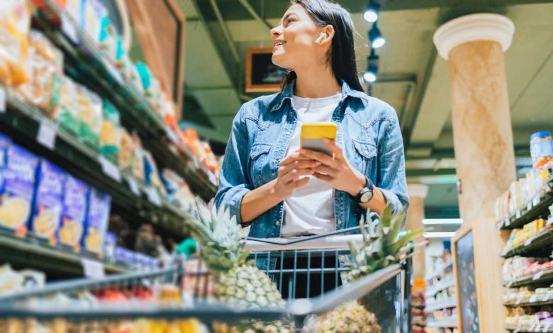 donna che fa la spesa al supermercato controllando la lista della spesa sul cellulare