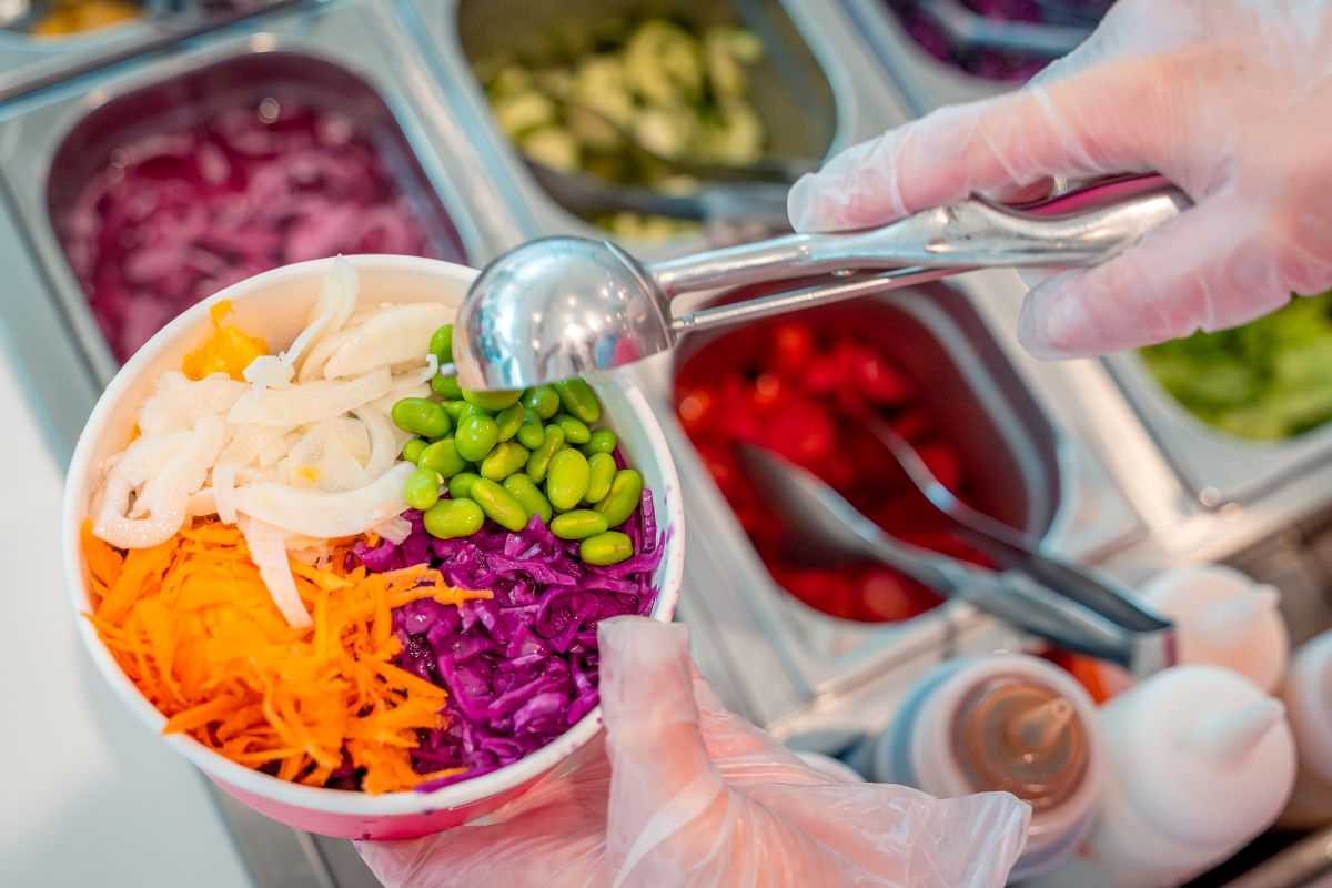 persona che compone un pokè inserendo gli ingredienti nella ciotola