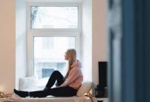 ragazza sola seduta vicino alla finestra di casa sua