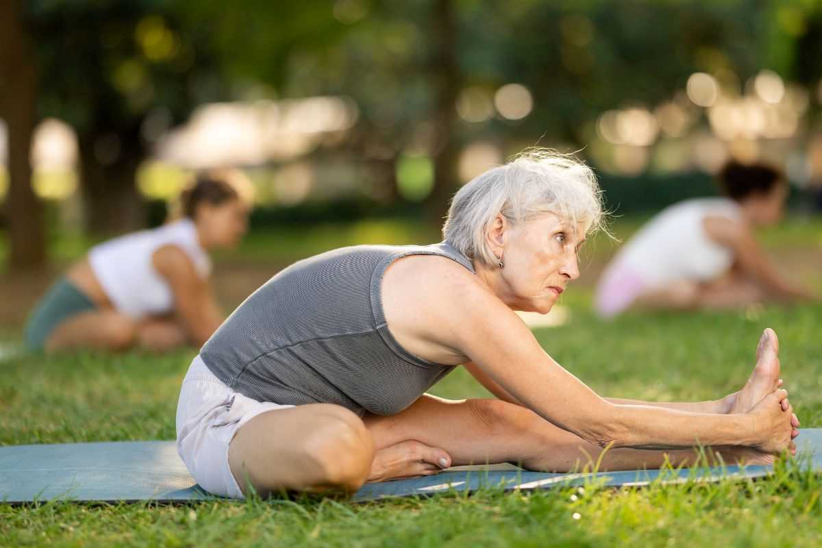 signora anziana che pratica yoga all'aperto in un prato