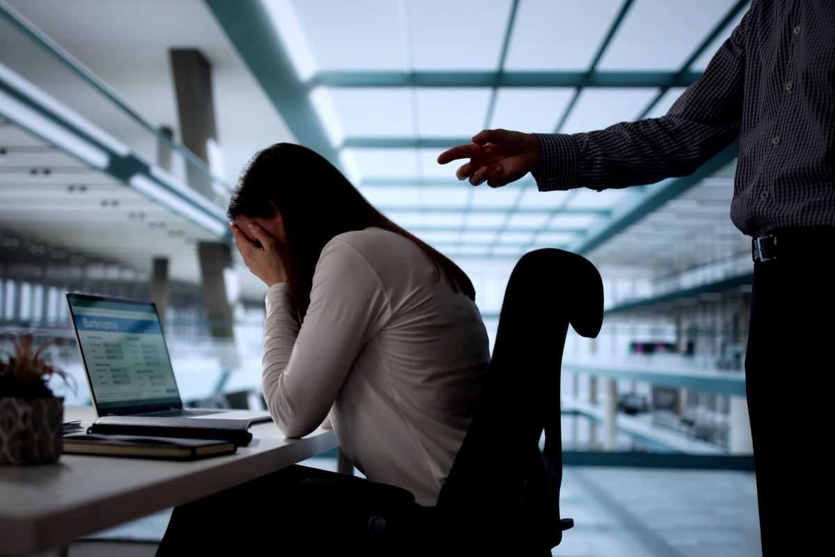 donna in ufficio con le mani sulla faccia mentre un collega le punta il dito addosso
