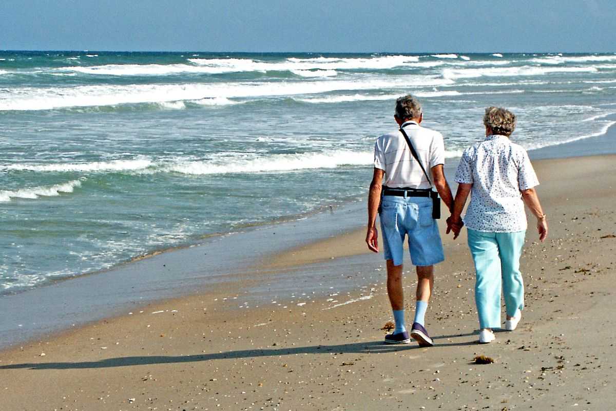 due anziani che passeggiano in spiaggia sulla battigia