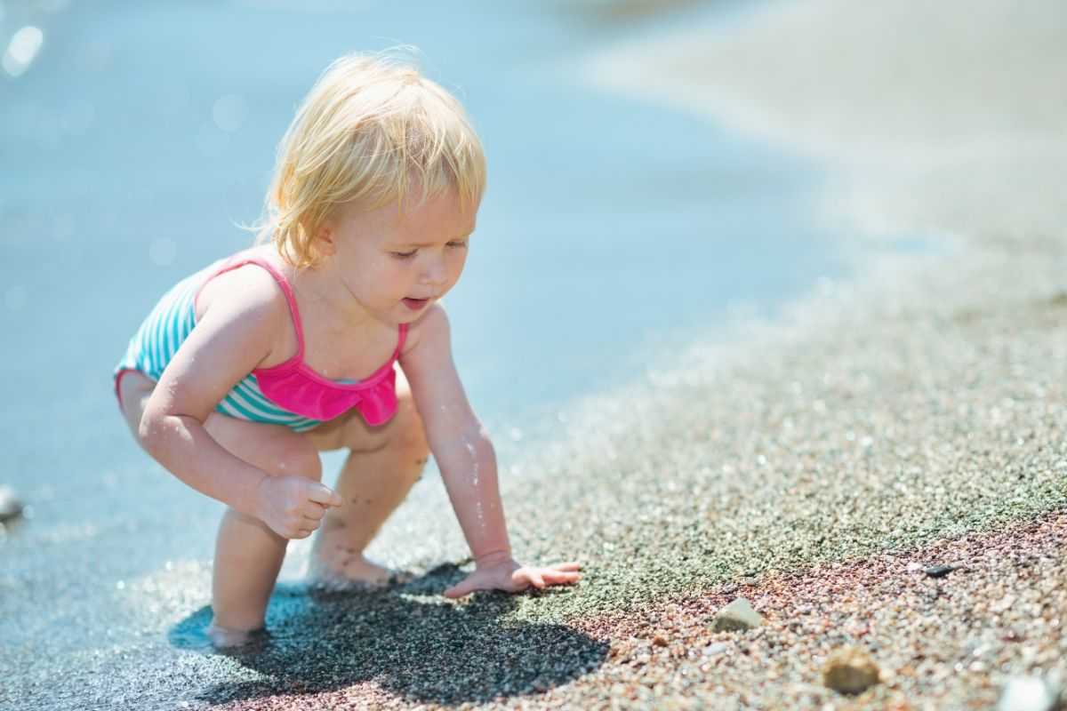 bambina che tocca la sabbia sulla battigia