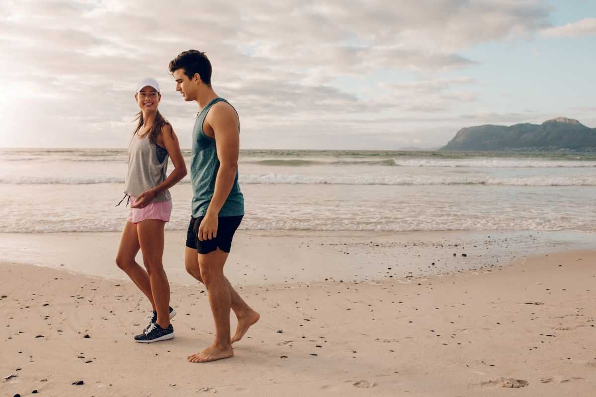 coppia che si allena in spiaggia senza attrezzi camminando sul bagnasciuga