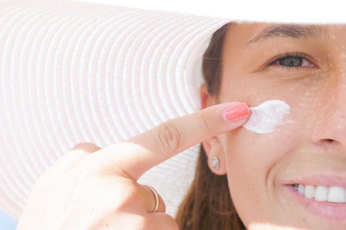 primo piano di donna che si applica la crema solare sul viso