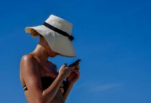donna in spiaggia che utilizza lo smartphone e non riesce a staccare la spina neanche in vacanza