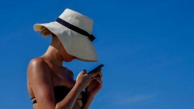 donna in spiaggia che utilizza lo smartphone e non riesce a staccare la spina neanche in vacanza
