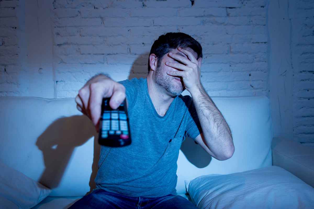 un uomo si copre gli occhi mentre guarda un film in televisione