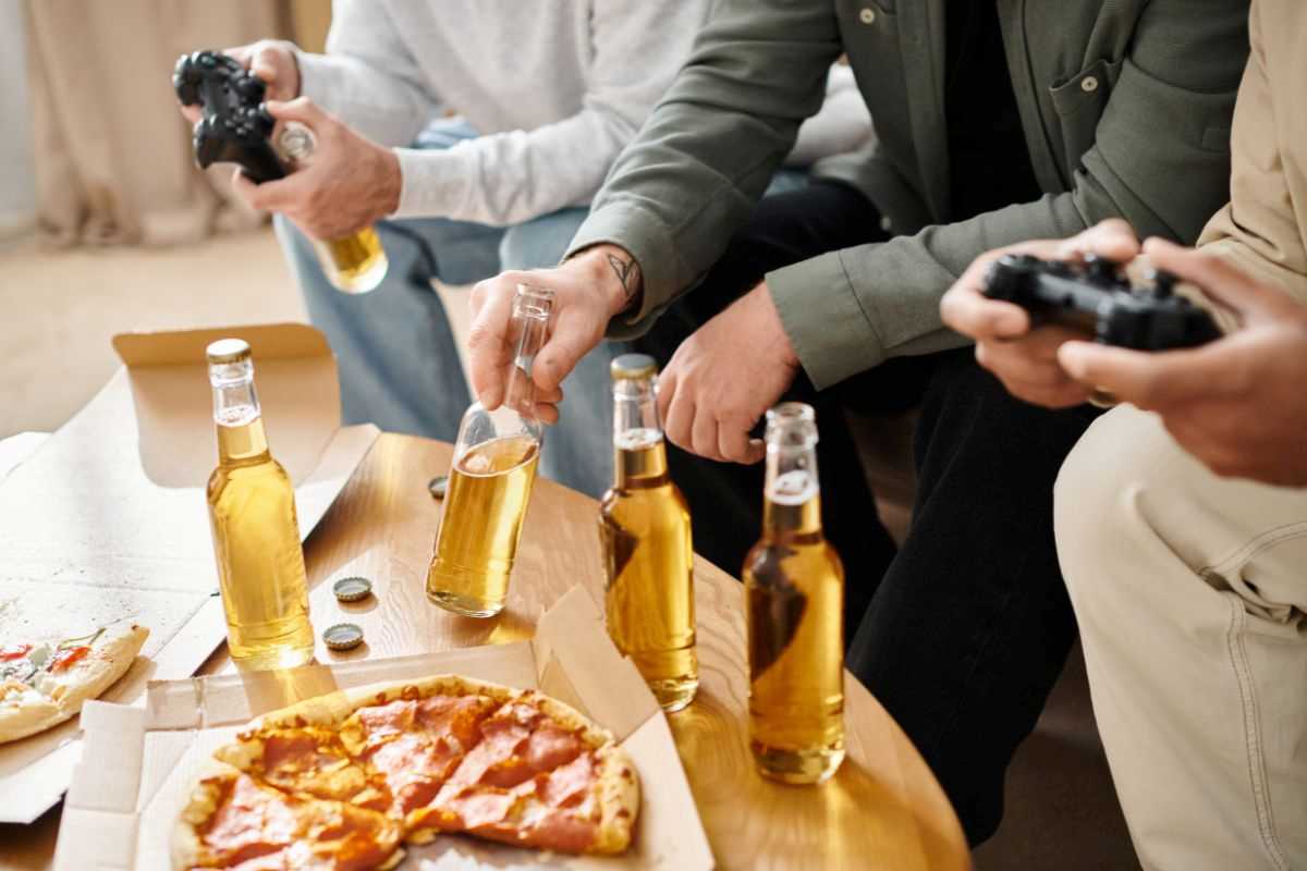 gruppo di amici che gioca ai videogiochi mentre mangia pizza e beve birra