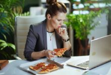 donna che mangia la pizza davanti al pc, una delle abitudini che fanno ingrassare