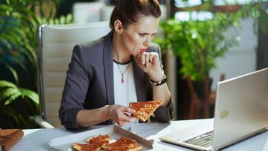 donna che mangia la pizza davanti al pc, una delle abitudini che fanno ingrassare
