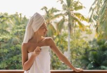 donna che si rilassa in accappatoio e turbante sui capelli mentre sorregge una tazza di te, su una terrazza immersa nel verde durante un retreat wellness