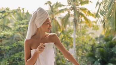 donna che si rilassa in accappatoio e turbante sui capelli mentre sorregge una tazza di te, su una terrazza immersa nel verde durante un retreat wellness
