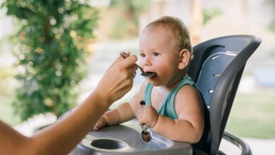 neonato seduto sul seggiolone che ha iniziato lo svezzamento e mangia dal cucchiaino offerto dalla mamma