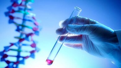 mano che regge una provetta con del sangue con un modellino di dna alle spalle