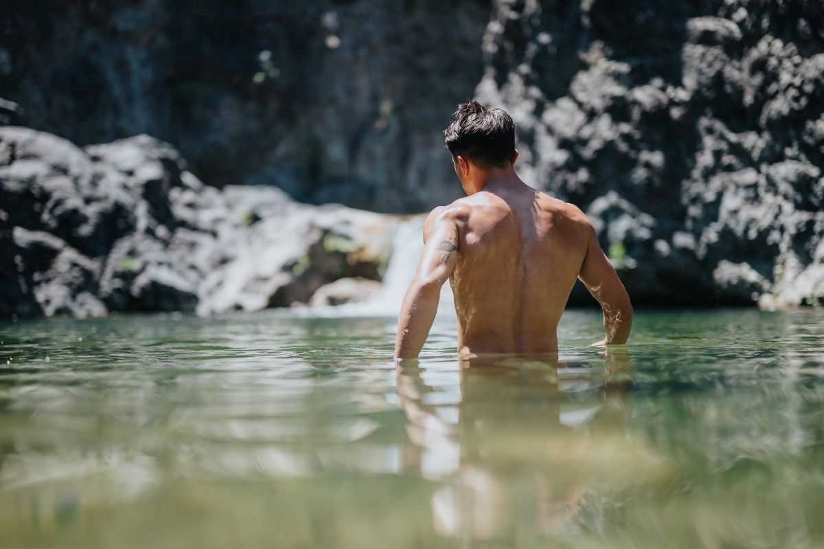 uomo di spalle immerso per metà in acque naturali in una baia