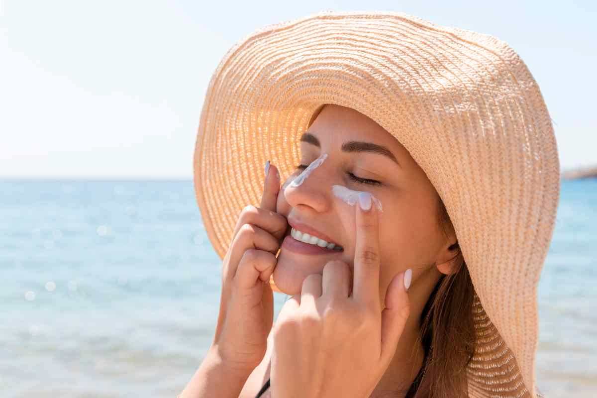 una ragazza con il cappello si mette la crema solare sul viso