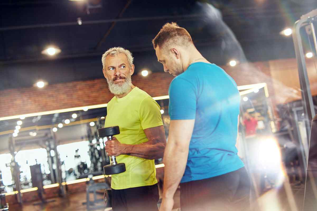 un uomo maturo si allena in palestra guidato da un personal trainer