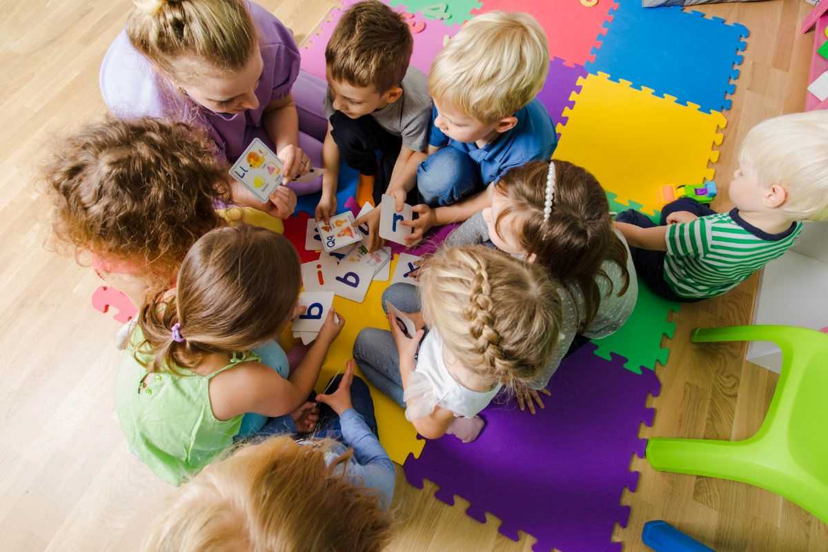 bambini all'asilo seduti in cerchio su un tappeto mentre guardano immagini di animali
