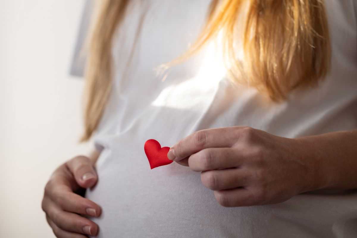 donna in gravidanza che appoggia un cuoricino di carta sul pancione