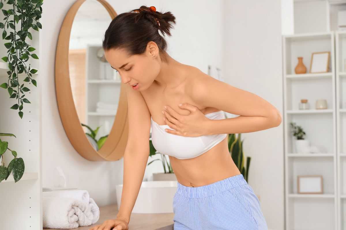donna che si appoggia al mobile del bagno mettendosi una mano sopra al seno perché sente dolore