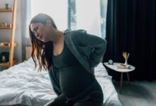 donna con tumore spinale in gravidanza che si siede sul letto a fatica perché sente dolore alla schiena