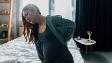donna con tumore spinale in gravidanza che si siede sul letto a fatica perché sente dolore alla schiena
