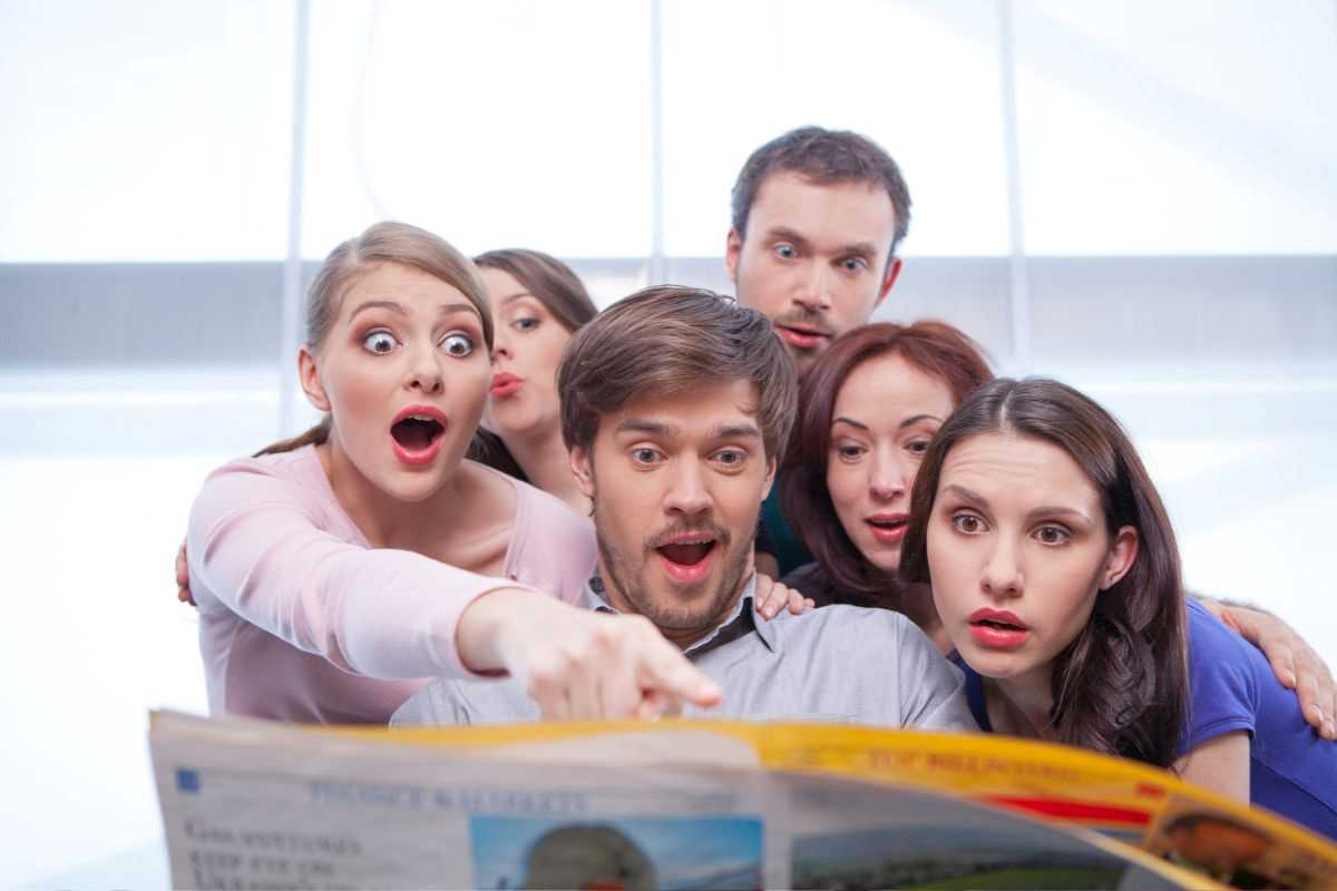 gruppo di persone che lgge un gossip su un giornale con facce stupite