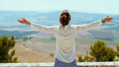donna di spalle che guarda un panorama con le braccia aperte
