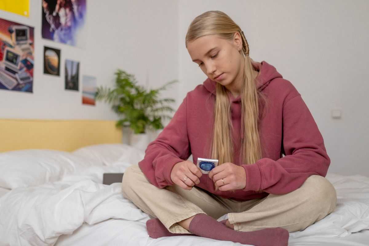 ragazza giovane seduta sul letto mentre tiene in mano un preservativo