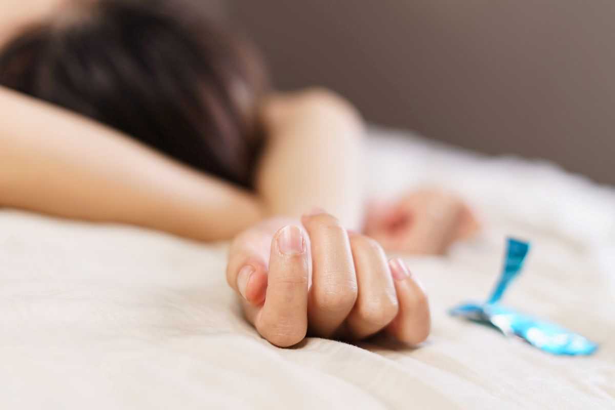 mano di donna sdraiata sul letto con affianco confezione preservativo aperta