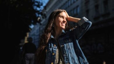 ragazza in città sotto al sole, sorridente, con mano appoggiata sull'occhio