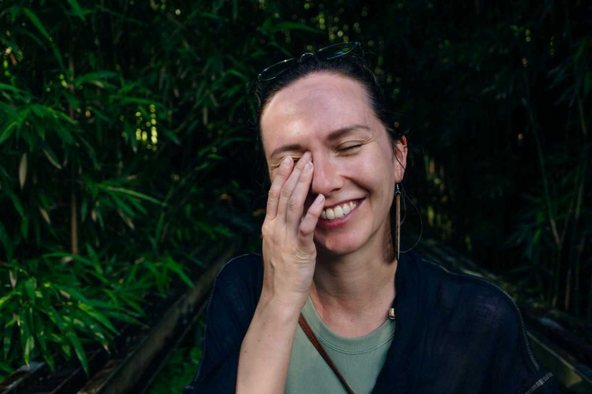 ragazza sorridente con occhi chiusi che appoggia una mano sull'occhio