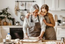 donna anziana che cucina mentre la figlia la abbraccia