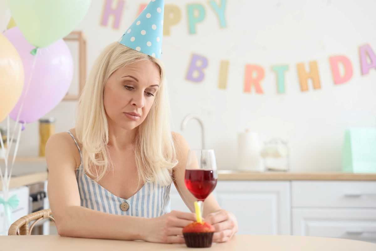 donna triste per aver compiuto gli anni con bicchiere di vino davanti a una tortina
