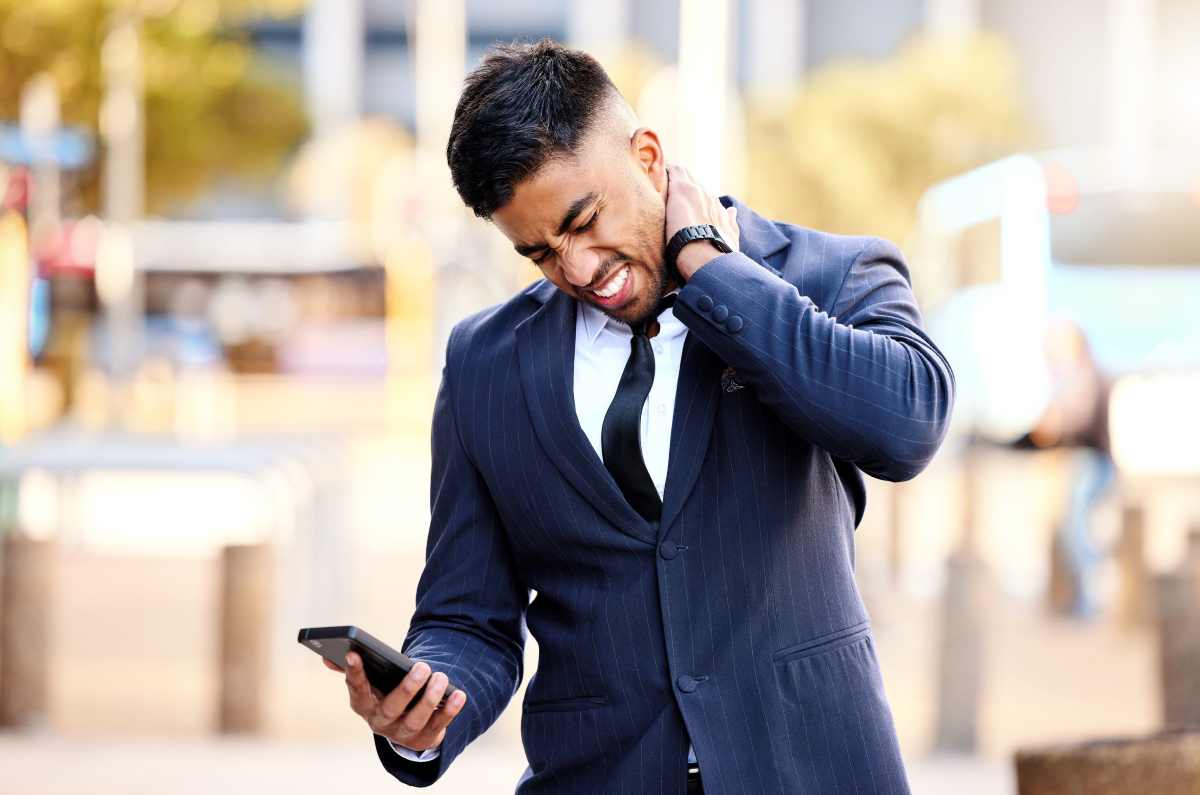 un uomo d'affari con il cellulare in mano si massaggia il collo dolorante